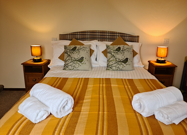 Double bedroom with towel-sets on the bed. Bother sides of the bed have bedside cabinets and table lamps.