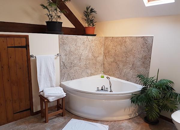 A corner bath and wooden side chair in a family bathroom.