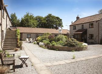 Barn conversions in a courtyard overlook a raised flower bed in its centre