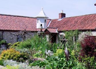 Exterior ofa barn conversion behind a shrub-filled garden.