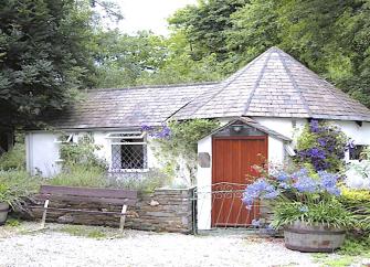 Exterior of a single-storey Cornish cottage surrouded by a tree-lined garden.