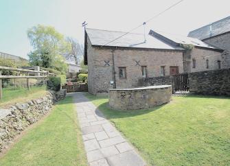 A large Exmoor Farm Cottage overlooks a lawn surrounded by a gated stone wall.