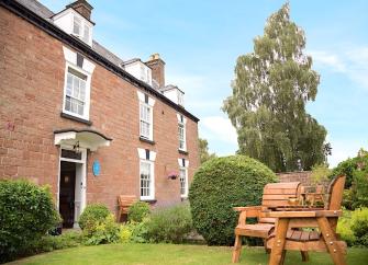 Exterior of a large, 3-storey, brick-built Wye Valley cottage with a large lawn.