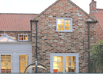 Exterior  of a brick-built, village holiday cottage and front garden at dusk.