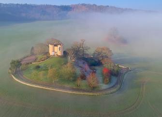 A mock Shropshire castle on a small hillock surrounded by a stone wall and open fields.