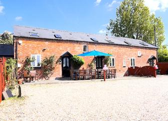 Exterior of a long brick-built barn conversion with a patio with table seating for 14.