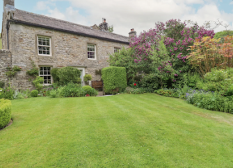 A large stone-built farmhouse overlooks a secure lawn and flower beds.