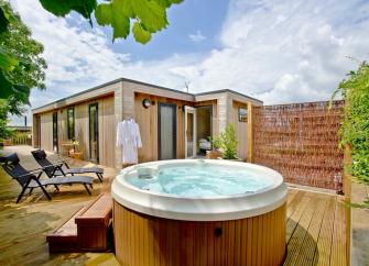 Exterior of a wooden eco lodge with a hot tub on its deck.