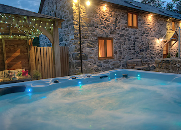 Illuminated hot tub at dusk facing a stone cottage with lights glowing in every window.