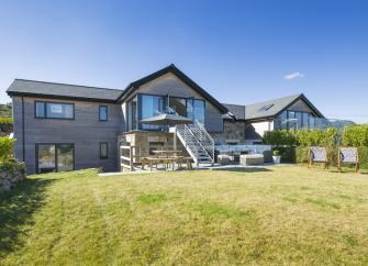 Exterior of a large timber lodge with a spacious deck overlooking an equally spacious, secure lawn.