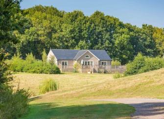 A timbered eco-lodge sits in front of mature woods overlooking open fields.