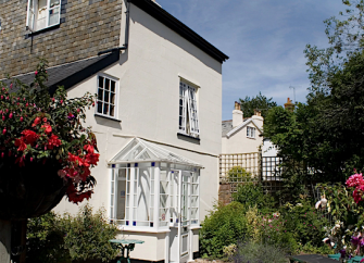 Exterior of a 3-storey cottage surrounded by beautiful flower-filled gardens.
