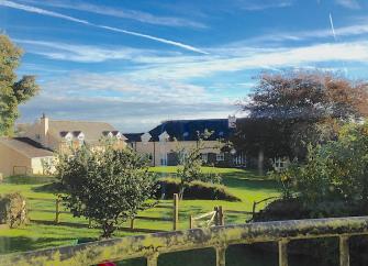 A large lawn with apple trees has a row of farm cottages in the background.