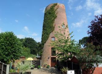 The tower of a windmill (no sails) surrounded by a shrub-filled garden.