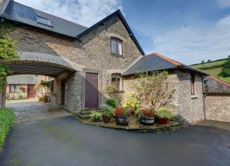 A stone-built cottage with a first floor that forms an arch over a driveway to a courtyard.