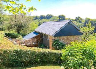 A soingle-storey, stone-built, Exmoor barn conversion surrounded by trees and hedgerows.