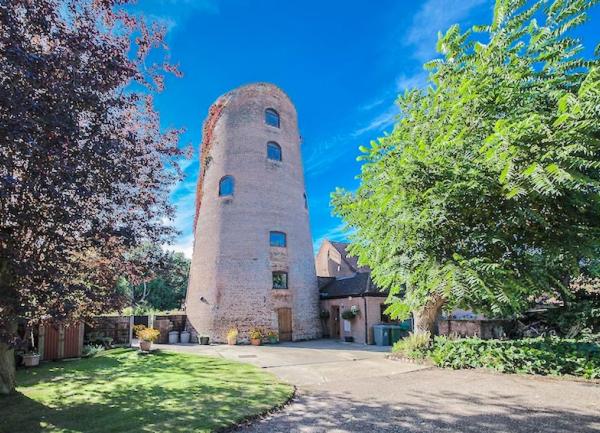 A converted windmll tower without and sails id flanked by mature treed.