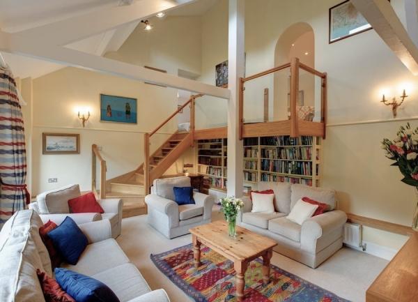 A high-ceilinged lounge with three large sofas, coffee table and a wide twin fully-stocked bookcase