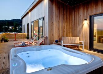 A hot tub and sunloungers on the deck of an timber eco lodge.