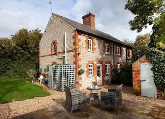 Exterior of a brick-built country cottage with a patio dining set on its courtyard.