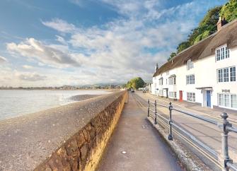 A terrace of thatched cottages overlook a road and beachfront at low tide.