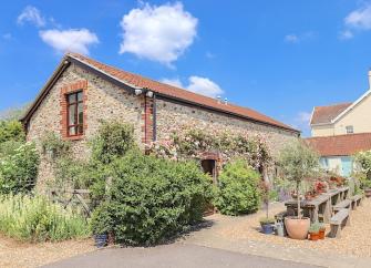 Exterior of a barn conversion with tables and chairs in a flower-filled courtyard.