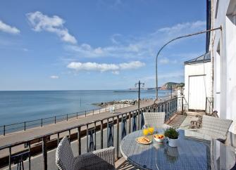 A balcony with table and chairs overlooks Sidmouth's seafront.