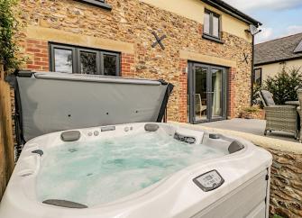 Exterior of a stone-built holiday cottage with a hot tub terrace.
