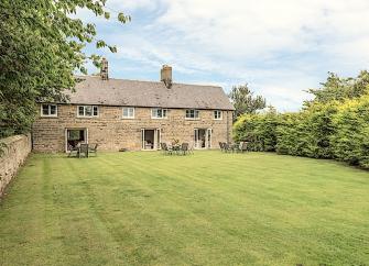 A long, stone-built cottage with 3 floor-to-ceiling ground-floor windows overlooking a spacious lawn. 