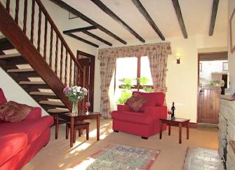 A lounge with armchairs, oak-beamed ceiling and a staircase.