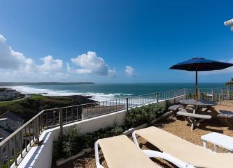 A view from sun loungers on a balcony to surf breaking on a beach in the distance.