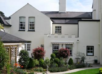 A large Regency cottage with large sash windows overlooks a flower-filled garden.