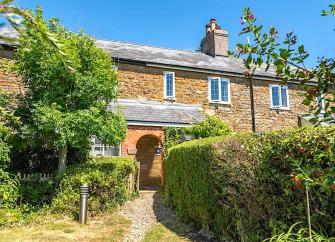 A footpath flanked by privet hedges leads to a stone-built holiday cottage with a covered porch.