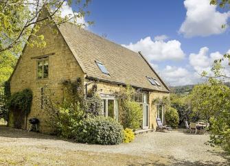 Cotswold Barn conversion surrounded by trees and shrubs.