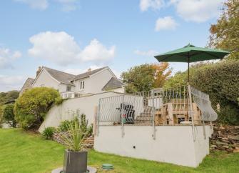 Exterior of a large contemporary house with a raised terrace and surrounded by mature gardens.
