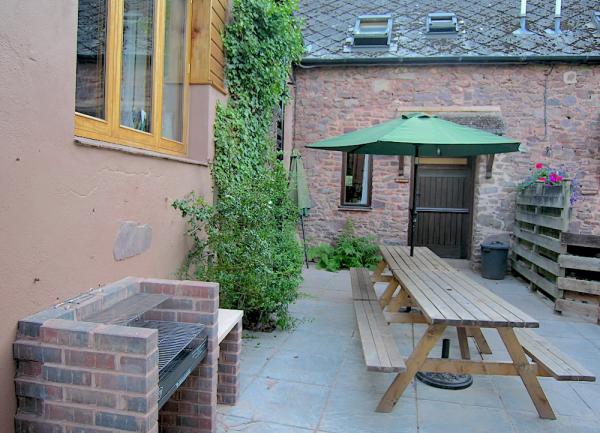 Patio with charcoal BBQ and large picnic bench with parasol.
