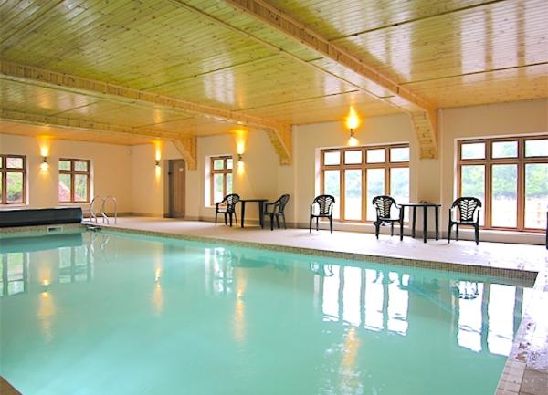 Large indoor heated swimming pool with poolside chairs.