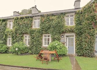 The ivy-clad exterior of a stone holiday cottage in Hawkshead, Cumbria, with a lawn to the front.