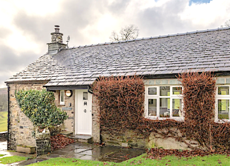 A stone-built,single storey holiday cottage with vine covered walls and a front garden.