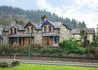 A twin gabled house with bay windows overlooks a railway line and fields.