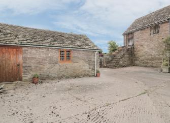 A single storey barn conversion stands on the edge of a paved courtyard.