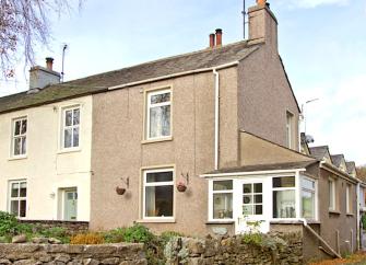 AW semi-detched cottage with enclosed front porch and a front garden behind a low stone wall.