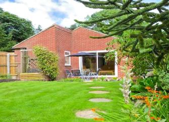 Rear exterior of a bungalow overlooking a tree-lined lawn.