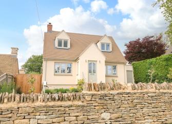 Exterior of a contemporary detached village house behind a dry stone wall.