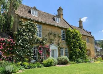 A stone-built house with roses and wisteria climbing the walls.