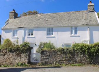 Quaint country cottage overlooks a garden surrounded by a stone wall.