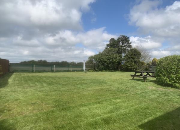 Large lawn with a picnic bench and lined by hedges.
