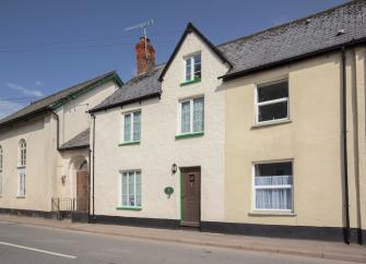 The exterior of a double-fronted terraced cottage overlooks an empty village street.