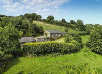 A remote hillside lodge on the side of a hill surrounded by fields, hedgerows and trees.