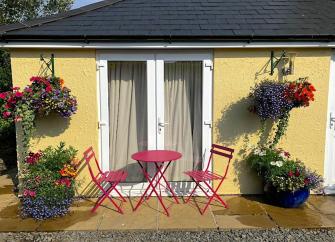 A single storey buikding with French Windows opening onto a terrace with floral hanging baskets